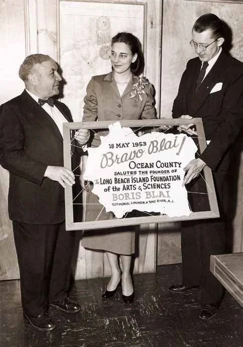 Three people holding a framed sign honoring LBIF founder Boris Blai in 1953.