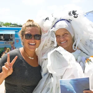 Two smiling women pose together at Barnegat Bay Day, one dressed in an outfit made entirely of plastic bags to raise awareness about pollution.