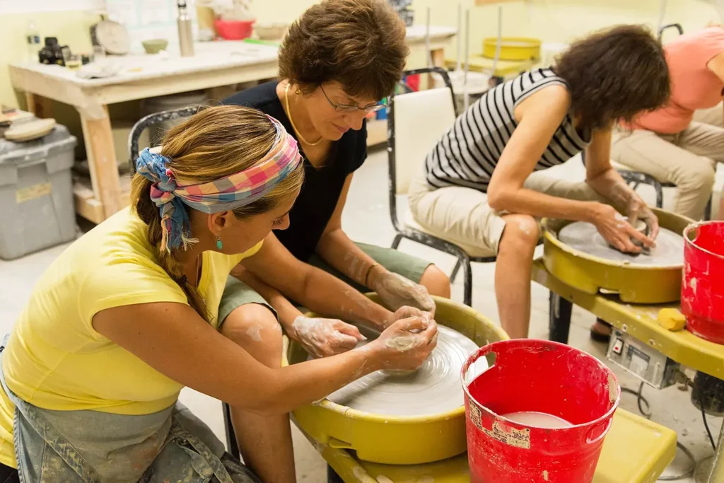 Ceramics instructor guiding a student at the pottery wheel during a class at LBIF.