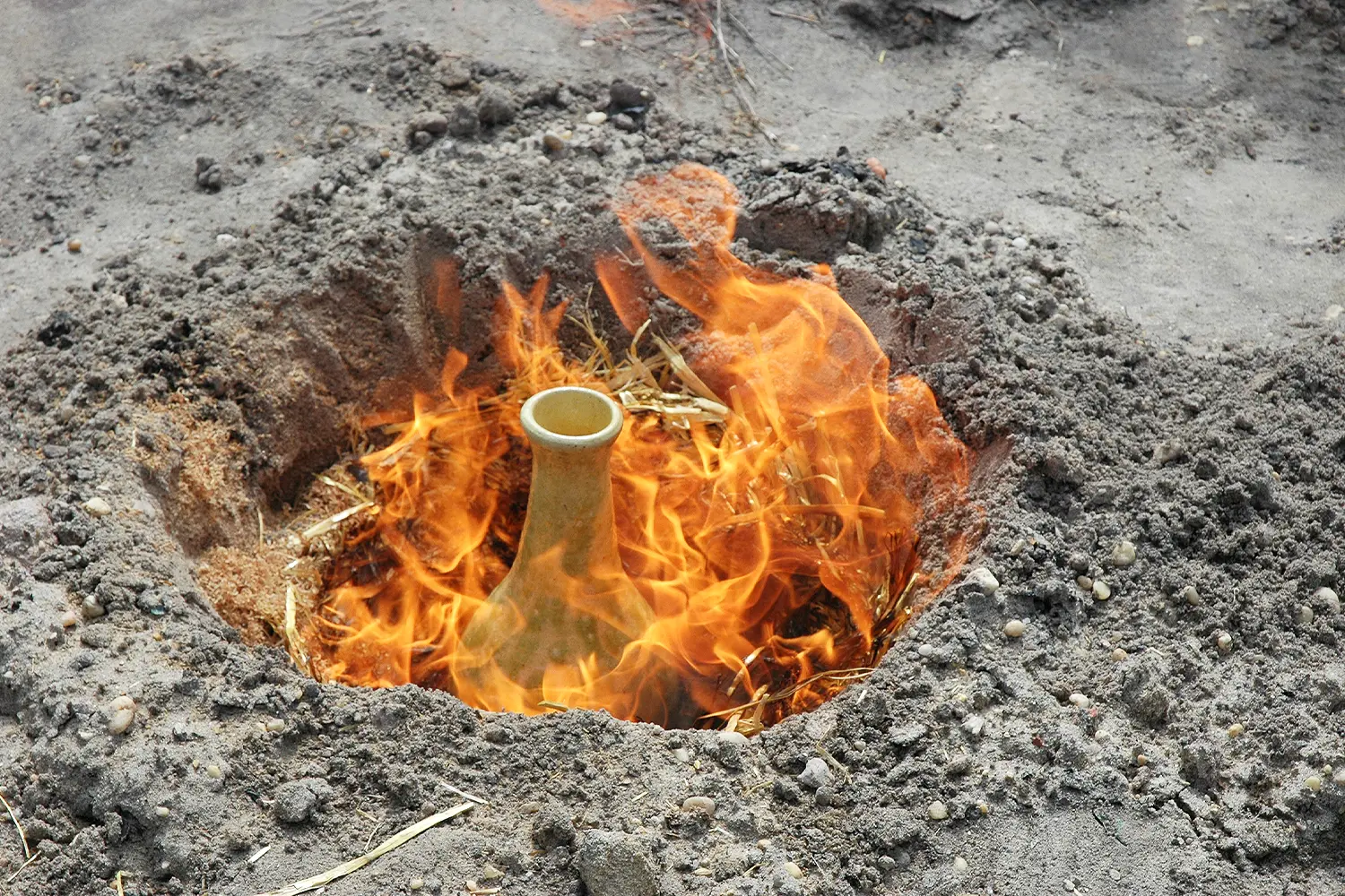 A ceramic vase being fired in a pit surrounded by flames and earth during a pit-firing process at LBIF.
