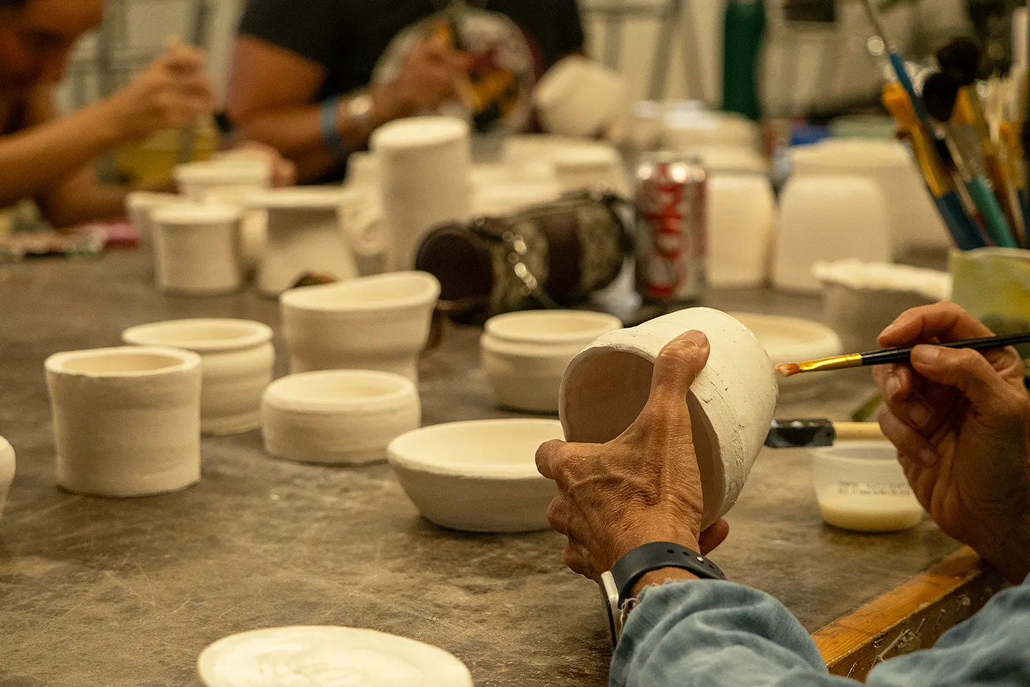 Hands painting a white ceramic bowl during a glazing session in the LBIF ceramics studio.