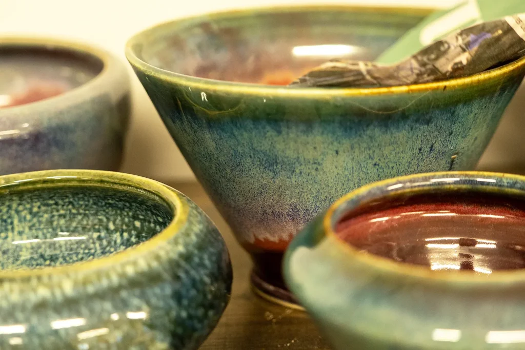 Close-up of handmade ceramic bowls with glossy blue-green and red glazes.