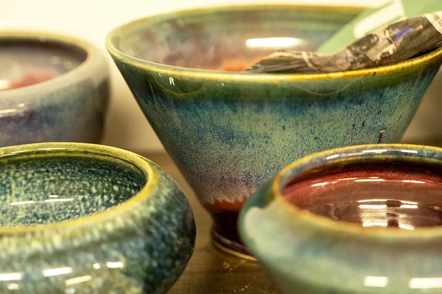 Close-up of handmade ceramic bowls with glossy blue-green and red glazes.