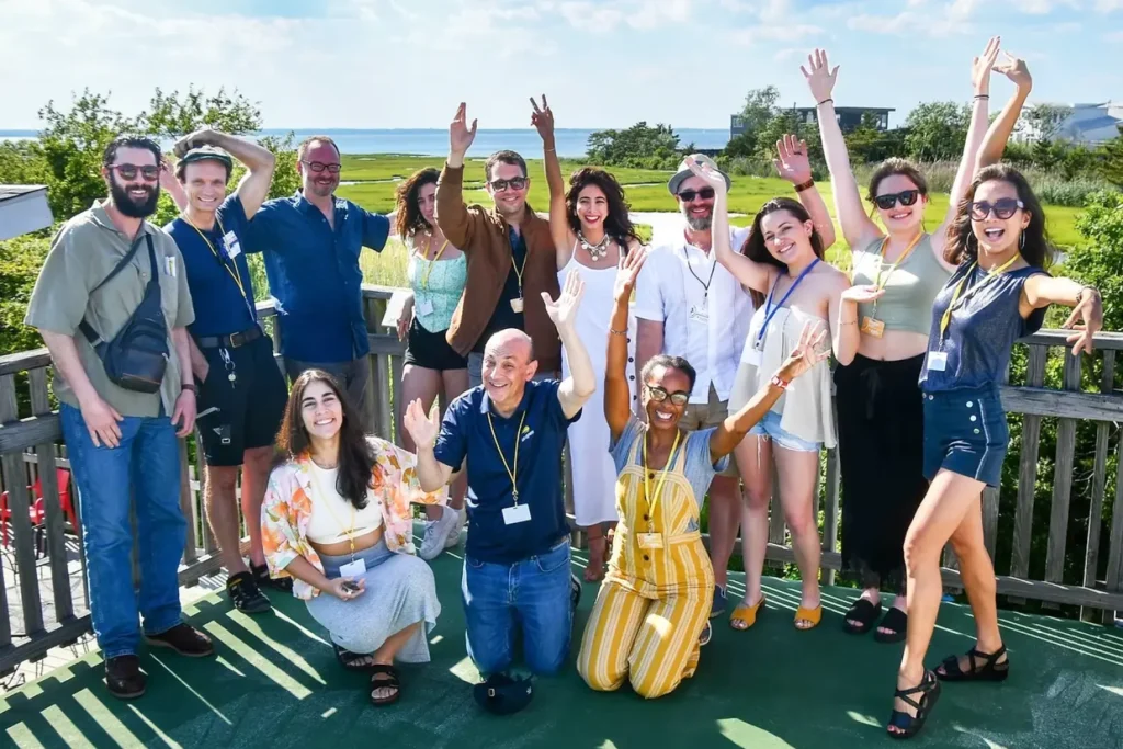 A group of smiling people pose together on an outdoor deck at the Long Beach Island Foundation, raising their hands in celebration with the bay and marshland in the background.