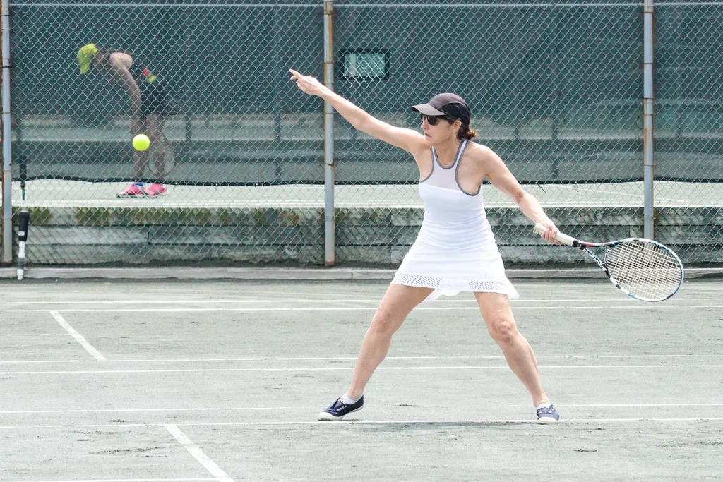 A woman in a white tennis outfit prepares to hit a forehand on the LBIF clay courts during a sunny match.