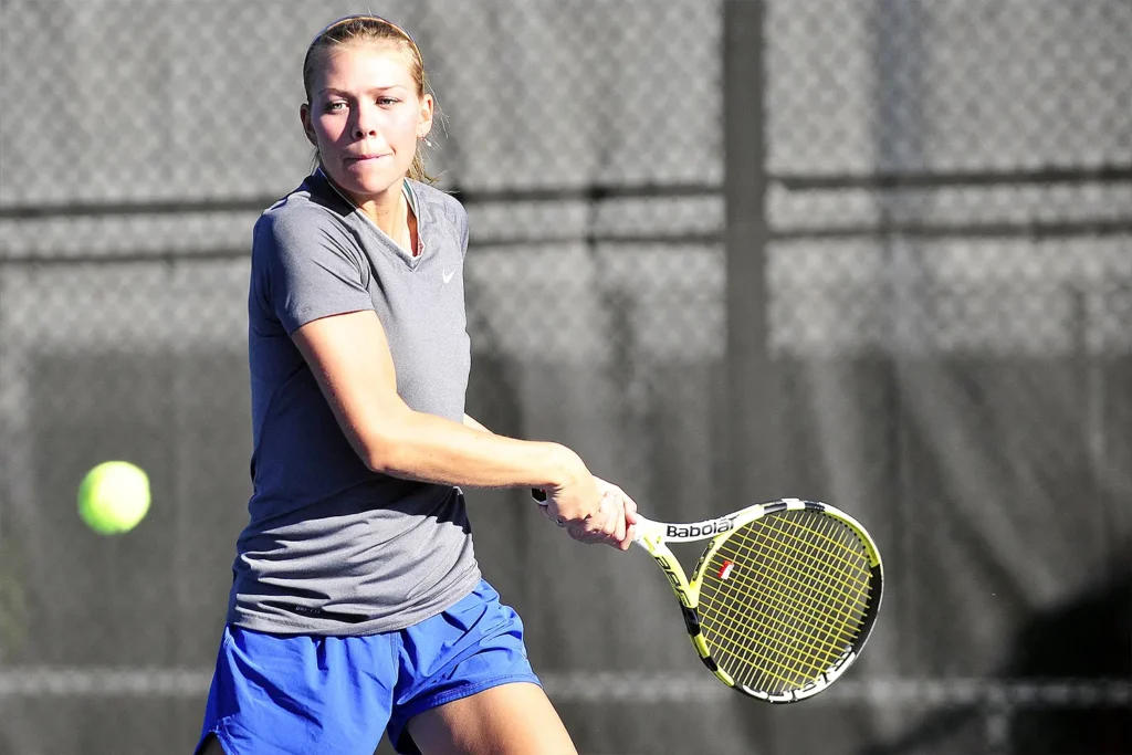 A woman prepares to hit a backhand shot during a sunny tennis match on the LBIF courts.