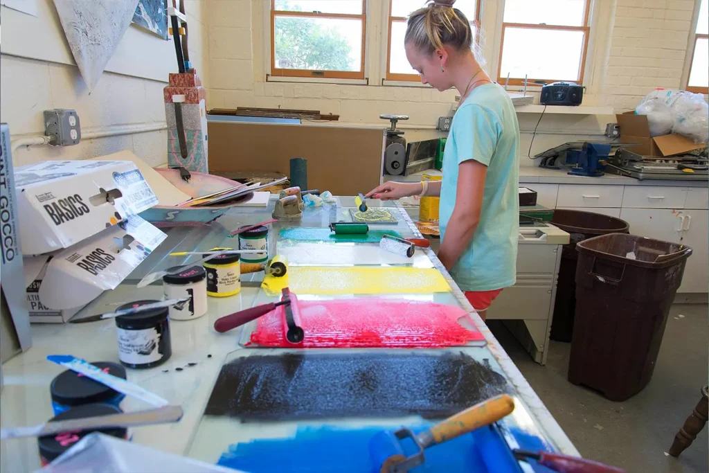 A camper works on a colorful printmaking project using rollers and bright inks in an art studio at LBIF.
