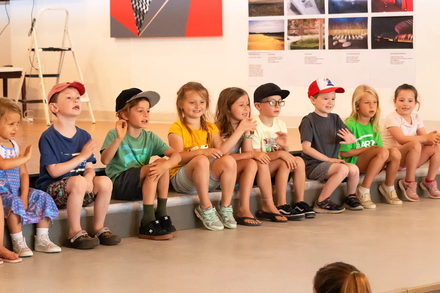 A group of young campers sits on a stage, smiling and gesturing with their hands during a group activity at the Long Beach Island Foundation of the Arts & Sciences.
