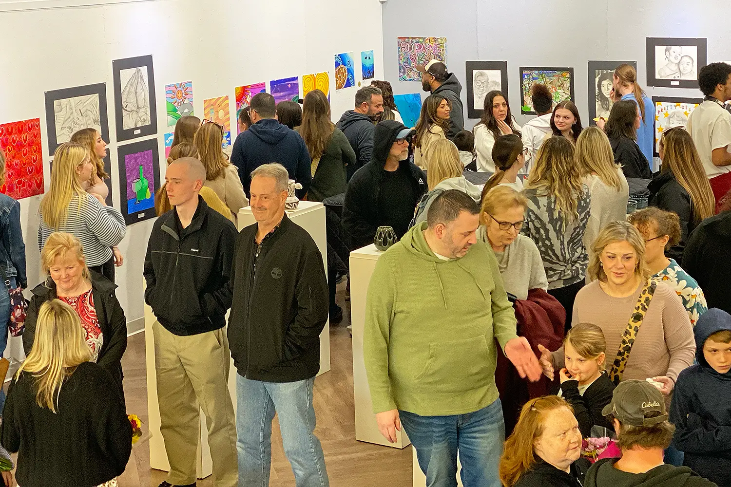 A crowded gallery at the Long Beach Island Foundation filled with students, families, and community members viewing colorful drawings and paintings at the Southern Regional High School Exhibition Reception.