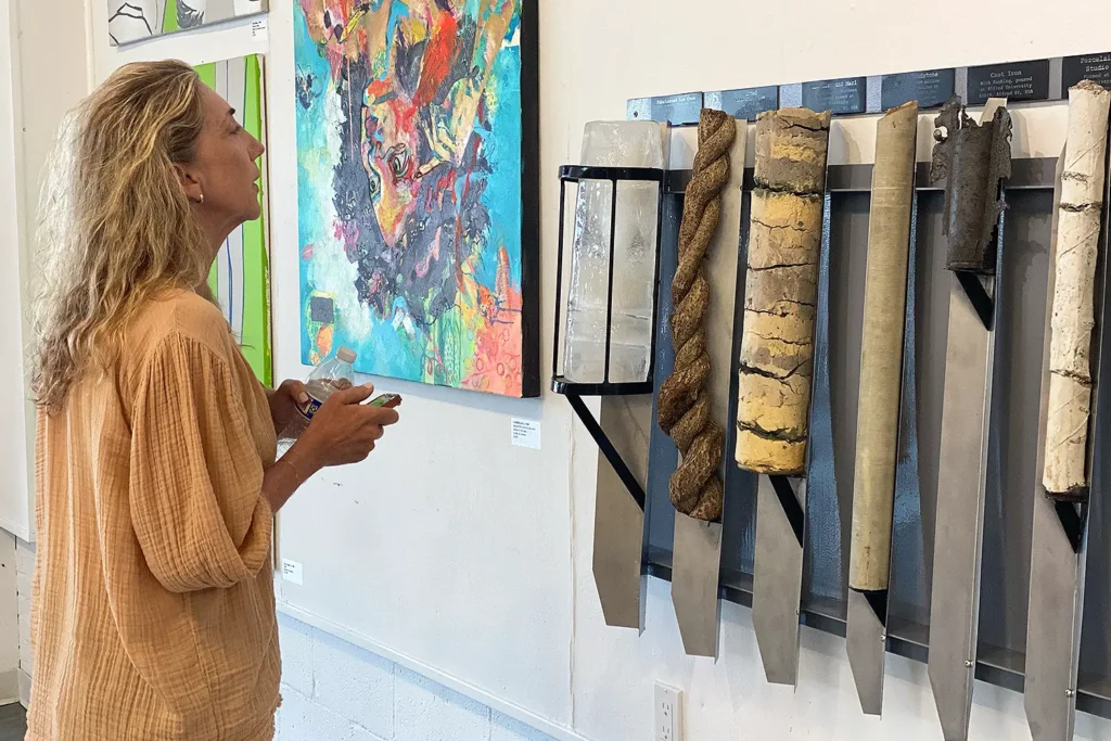 A woman observes an art installation featuring sculptural cores and a colorful abstract painting in a gallery setting.