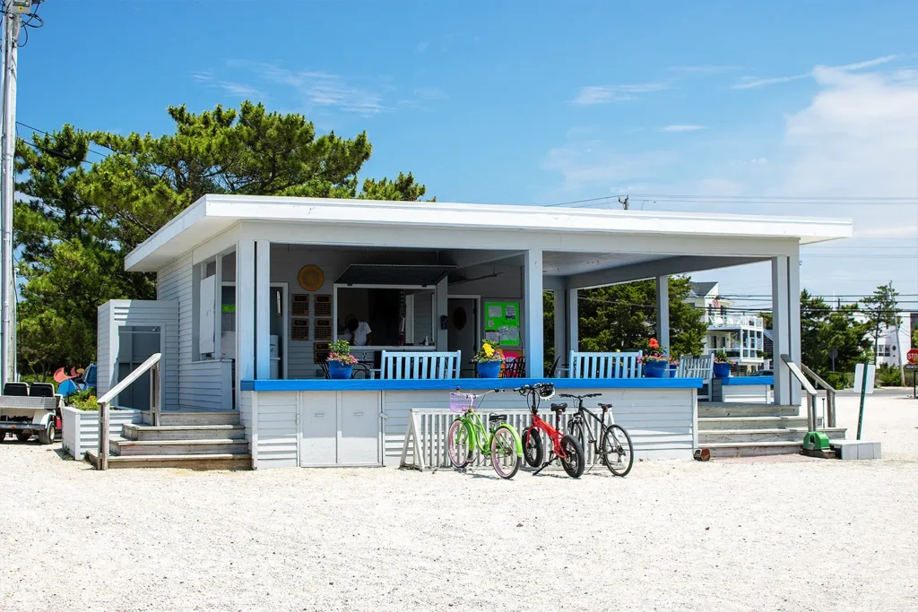 The Tennis and Pickleball Pavilion at the Long Beach Island Foundation of the Arts & Sciences, featuring a light blue building with covered seating areas, bicycles parked out front, and potted flowers adding color to the summer scene.