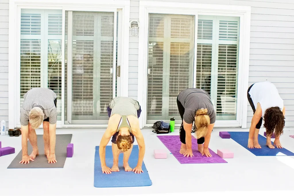 A small group of people practicing yoga in a forward fold pose on mats outside the LBIF pavilion, with yoga blocks and water bottles beside them.