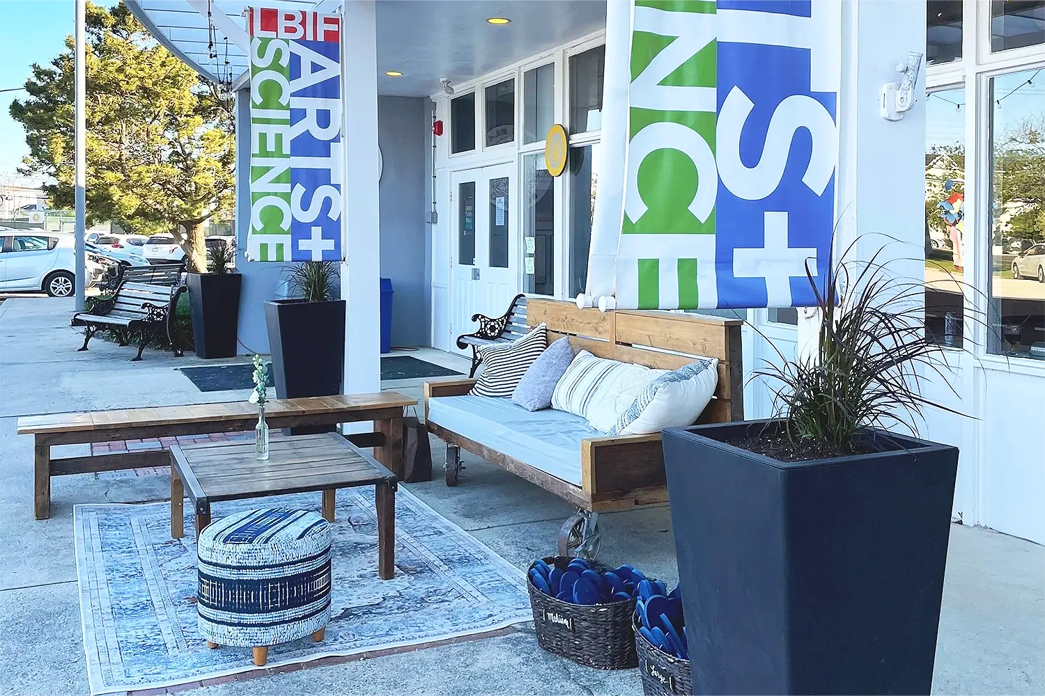 Outdoor seating area at LBIF Arts & Sciences set up for a private event, featuring wooden lounge furniture, planters, and Arts + Science banners at the entrance.