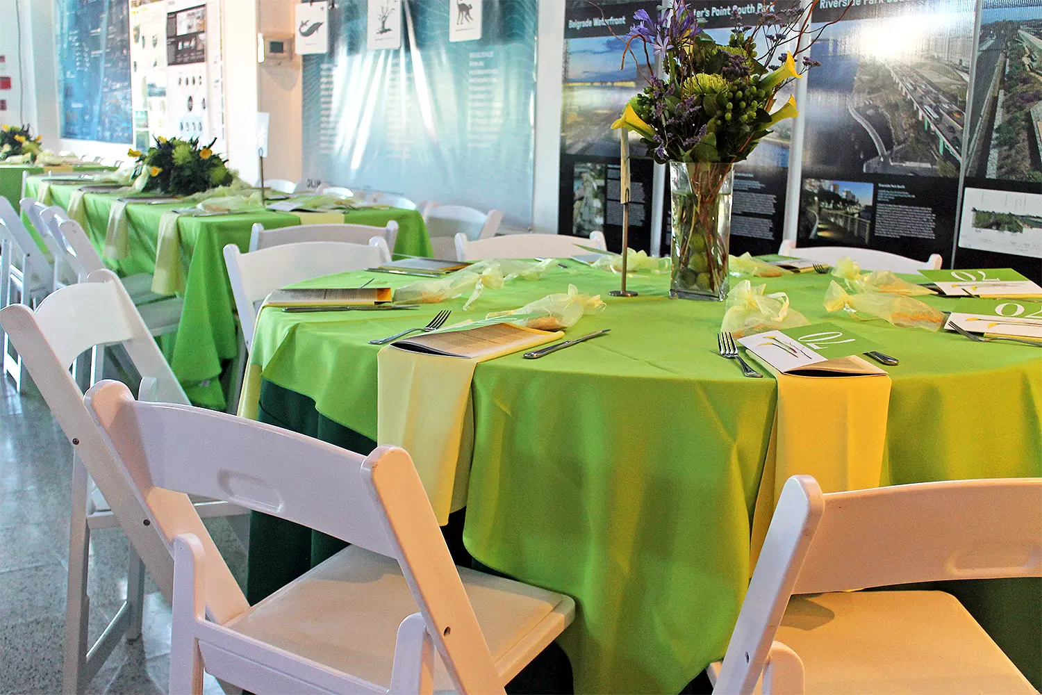 Round tables with bright green linens and white folding chairs set for a private event, featuring floral centerpieces and place settings.