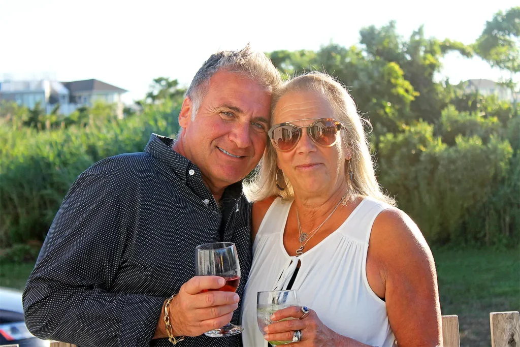 A smiling couple stands outdoors holding drinks during a sunny event.