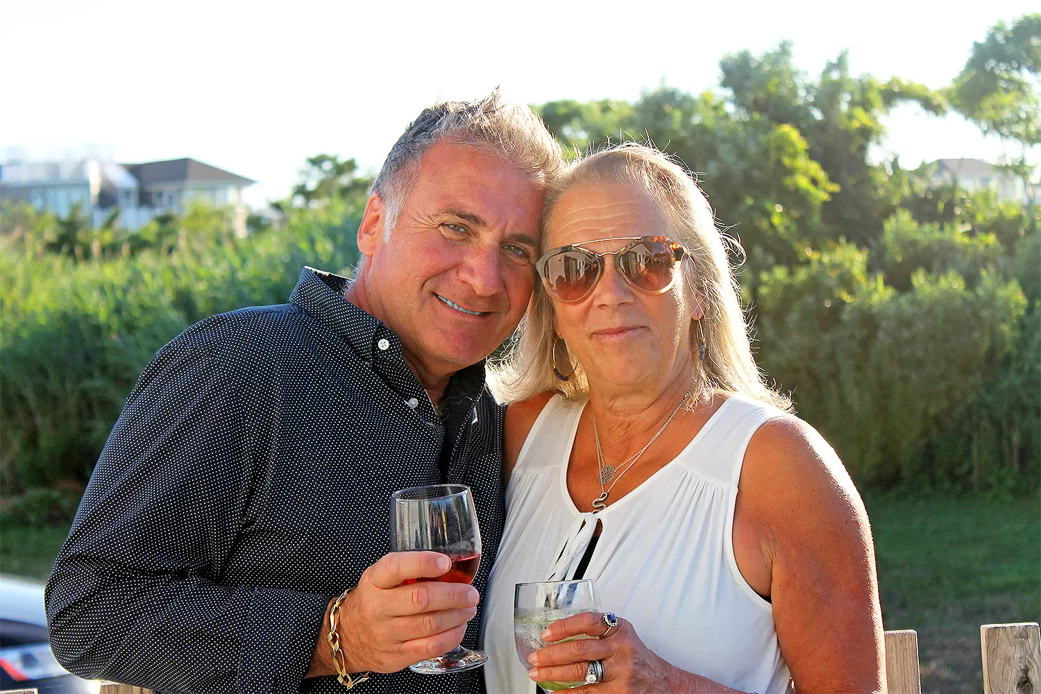A smiling couple stands outdoors holding drinks during a sunny event.