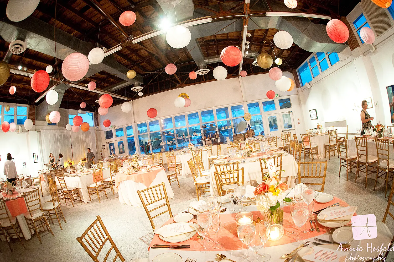 Wedding reception set inside the Long Beach Island Foundation of the Arts and Sciences with round tables, floral centerpieces, gold chairs, and hanging paper lanterns.