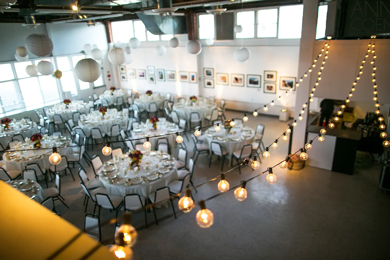 Wedding reception setup inside the Long Beach Island Foundation of the Arts and Sciences with round tables, string lights, and hanging paper lanterns.